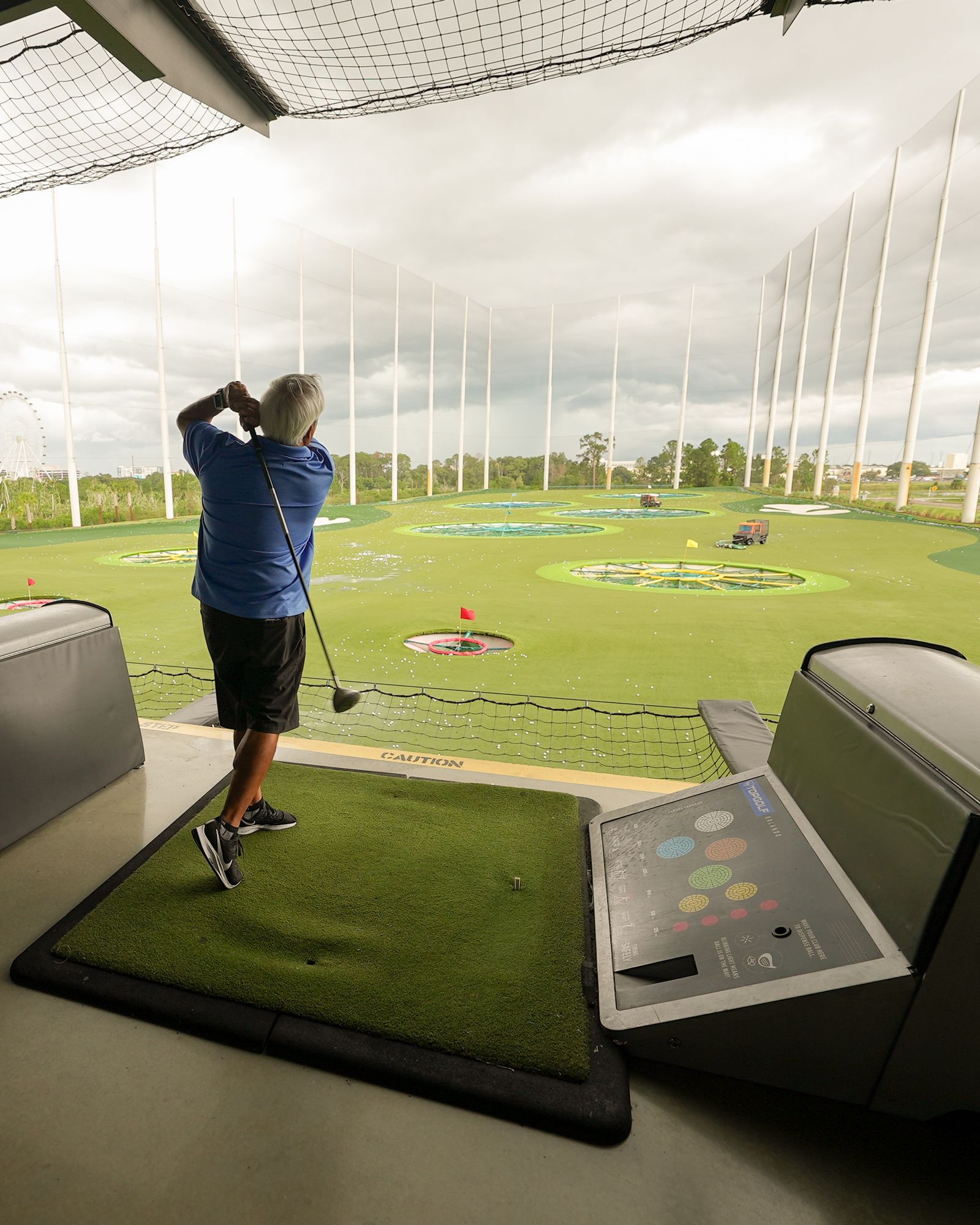Silver-haired golfer swinging a club at an indoor driving range