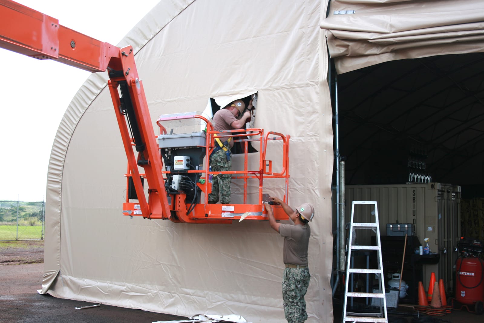 A crew stretching a new fabric skin over a steel-tubed tent frame