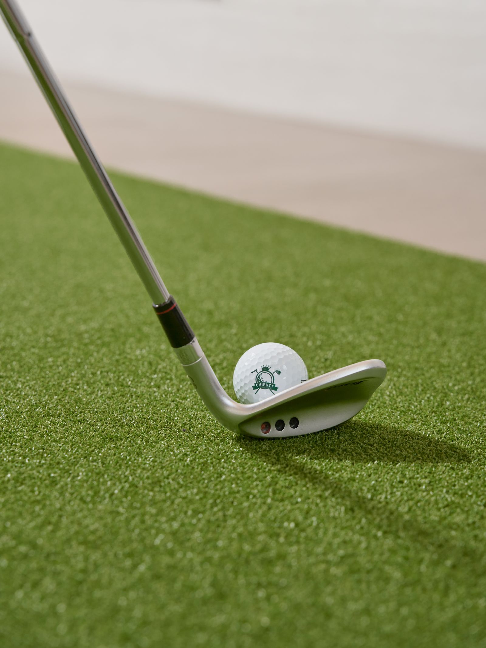 A golf club addressing a ball on artificial turf