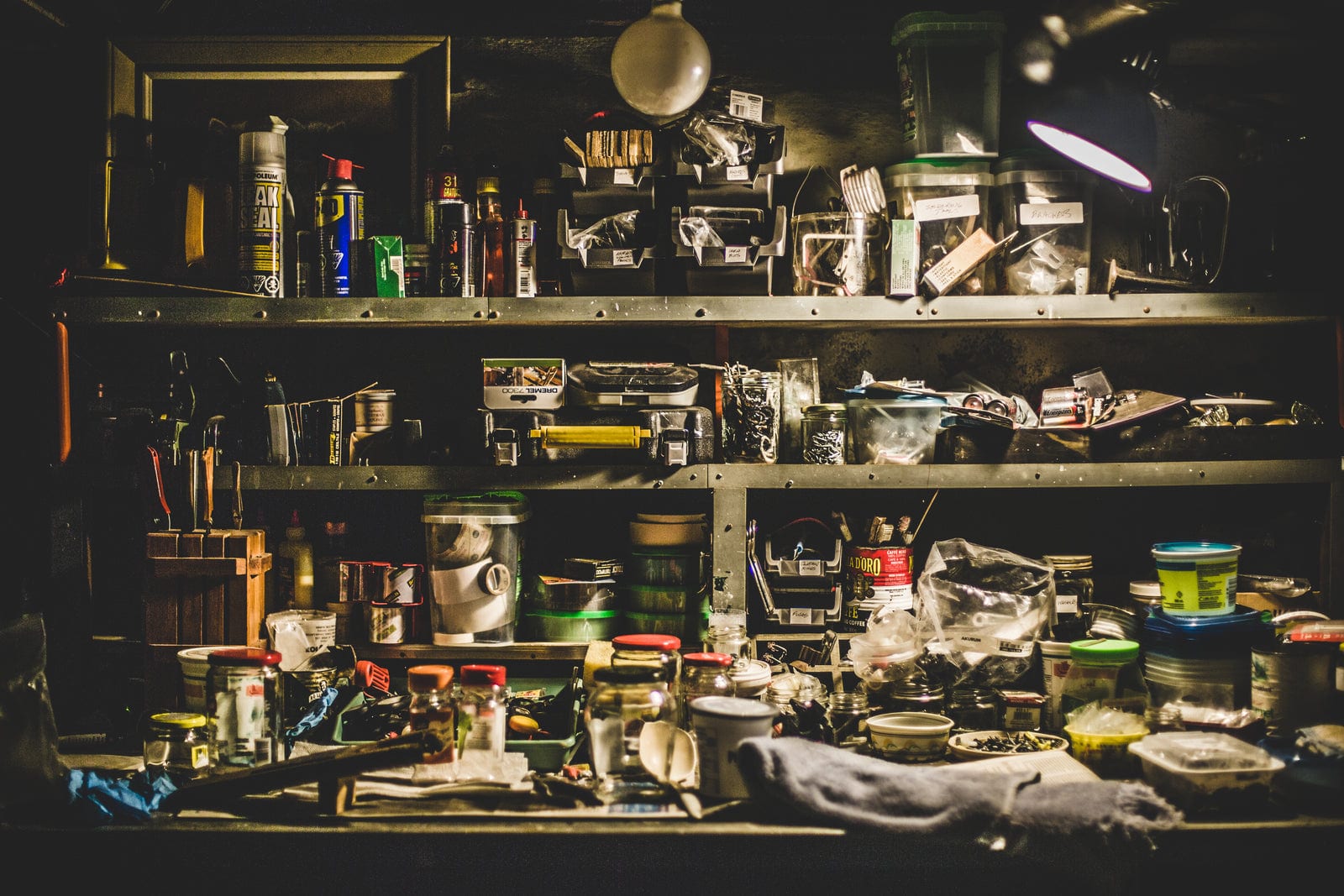 Cluttered workshop shelving in a garage, tools and hardware stored along the wall