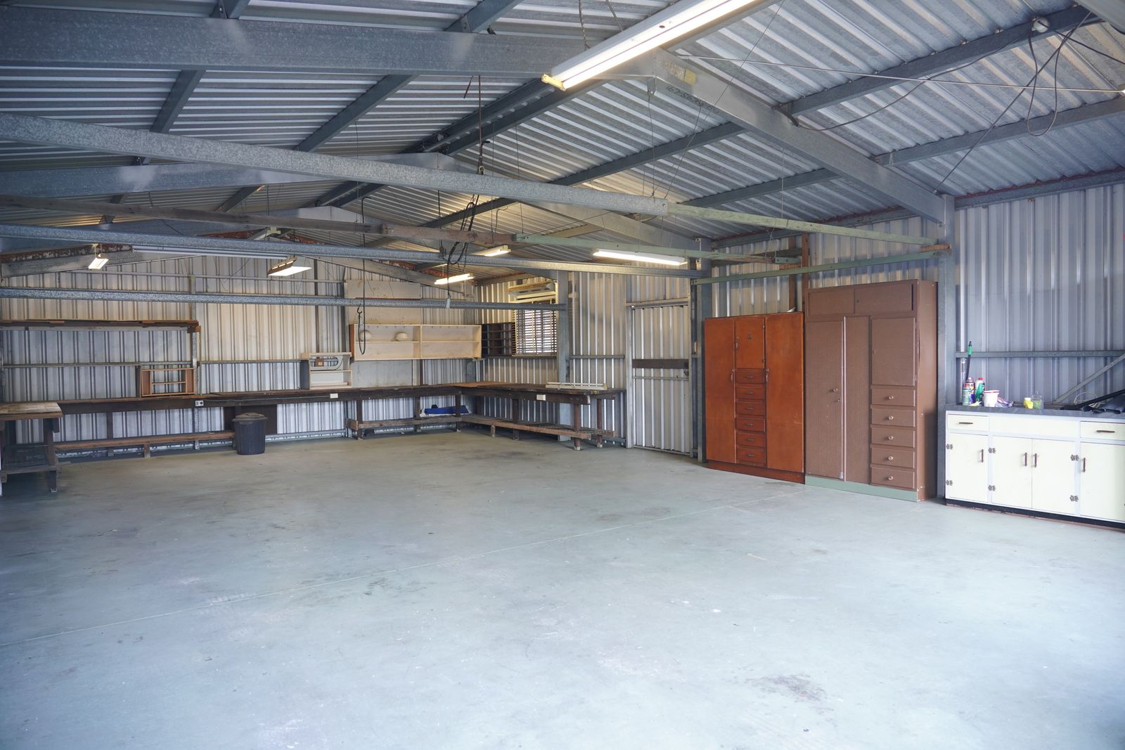 An empty garage bay with steel walls and ceiling, storage cabinets and workbenches along the sides.