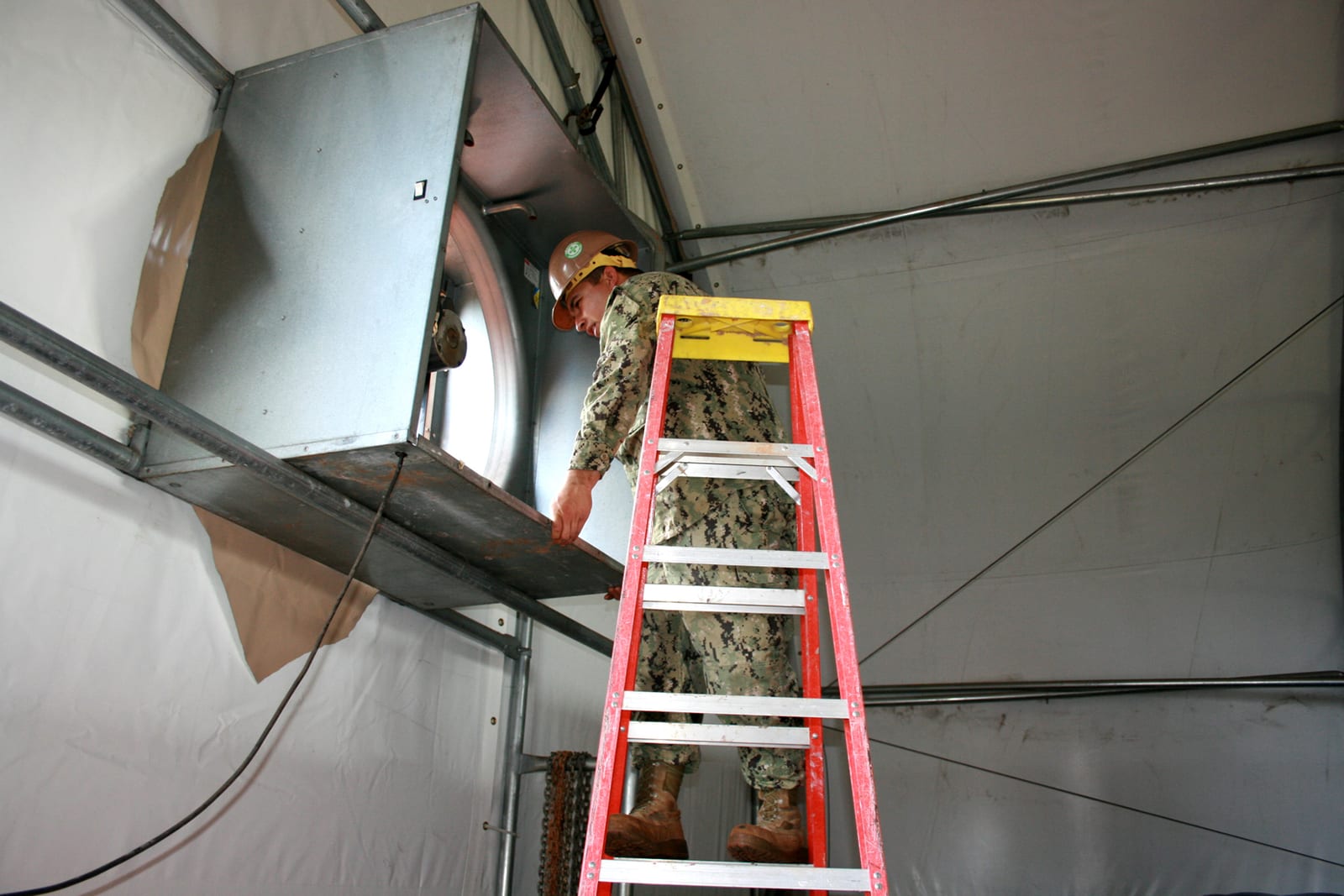 A crew installing an exhaust fan through a tent's steel-tubed frame and fabric skin