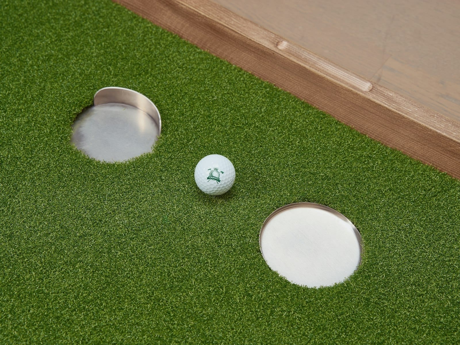 A golf ball resting between two metal putting cups on green indoor turf