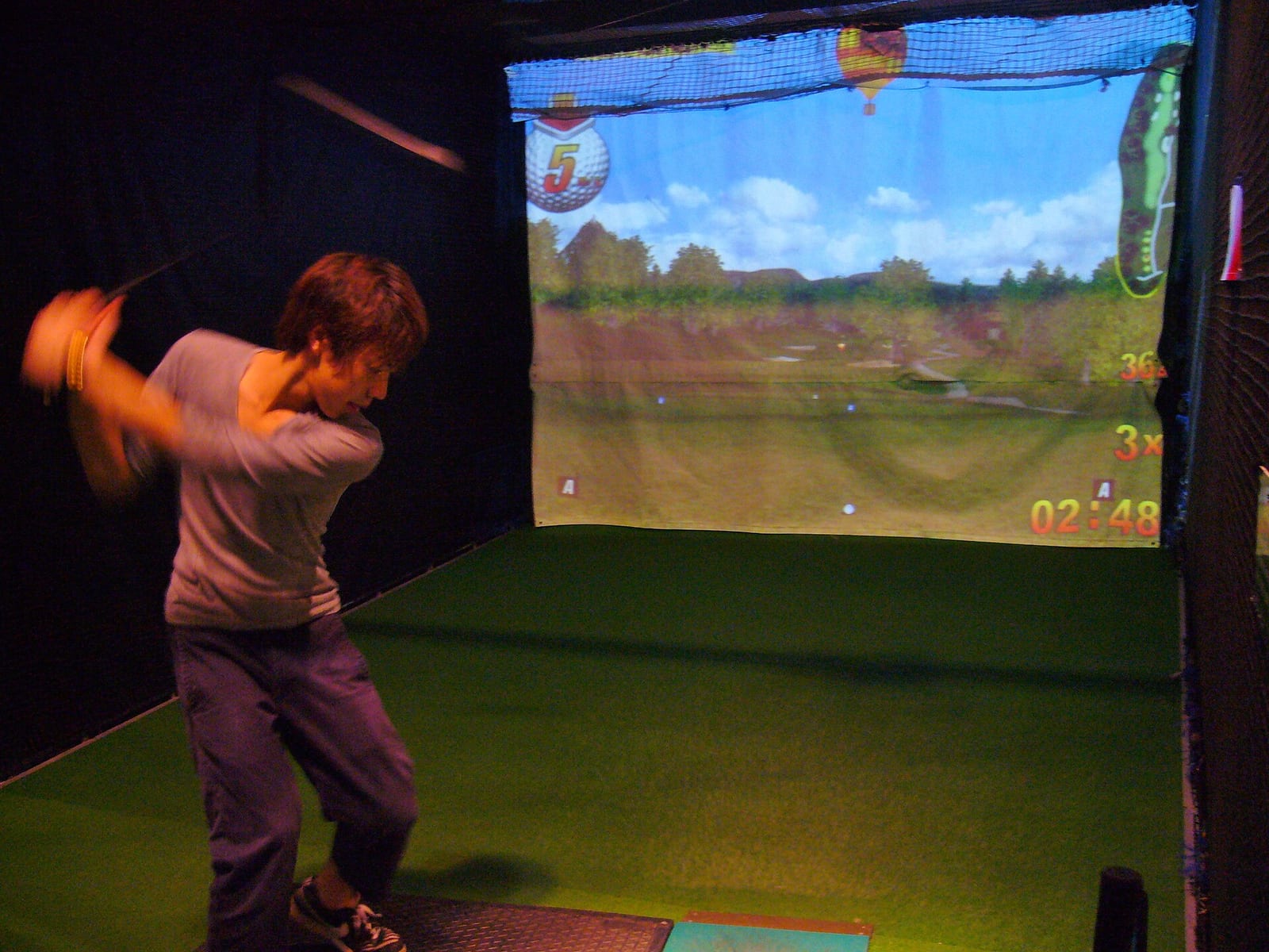 An indoor virtual golf driving range bay, golfer hitting into a projected course screen
