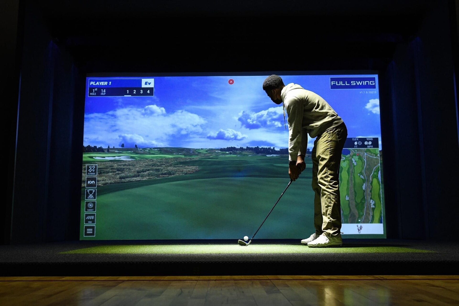 A service member swings a golf club into a Full Swing Elite golf simulator screen